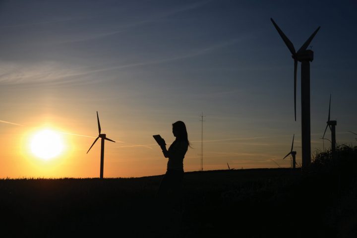 silhouette of woman holding book near windmills