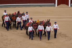 men in white shirts leading horses at bullring