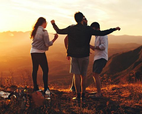 four person standing at top of grassy mountain
