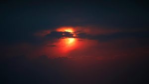 the sun is setting behind clouds in a dark sky